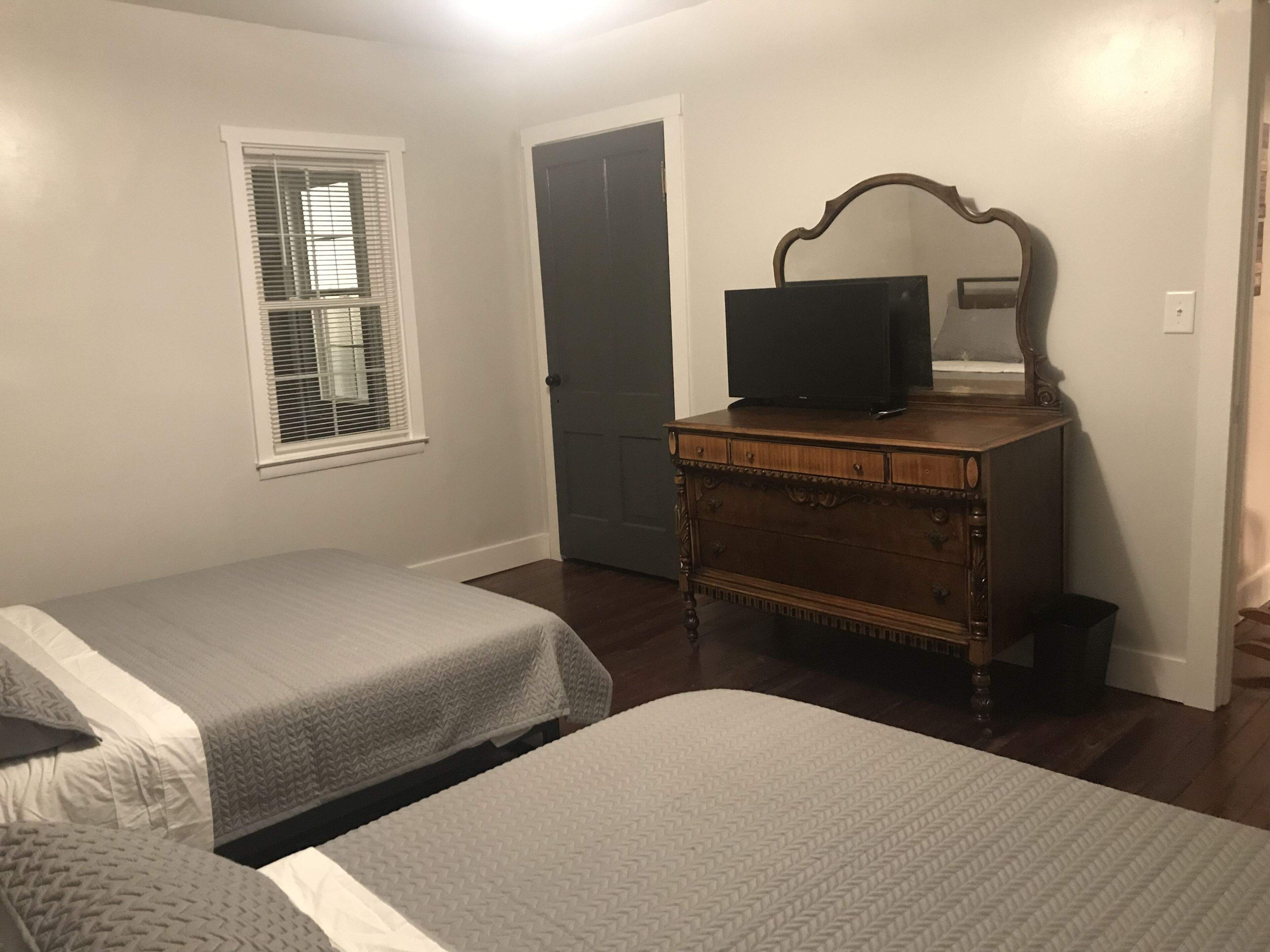 Un dormitorio con dos camas, un aparador, un televisor y una puerta.