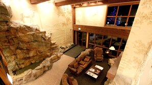 Un hall d’entrée spacieux avec un grand mur d’escalade, un coin salon avec un canapé et des fauteuils, et une vue sur le sapin de Noël installé à l’extérieur.