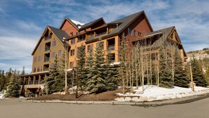 Un chalet à étages doté d’une façade en bois remarquable, de nombreux balcons et, en arrière-plan, d’une piste de ski.