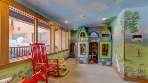 Un espace de jeux pour enfants comprenant une maison de jeu, des fauteuils à bascule et une vue sur l’extérieur.