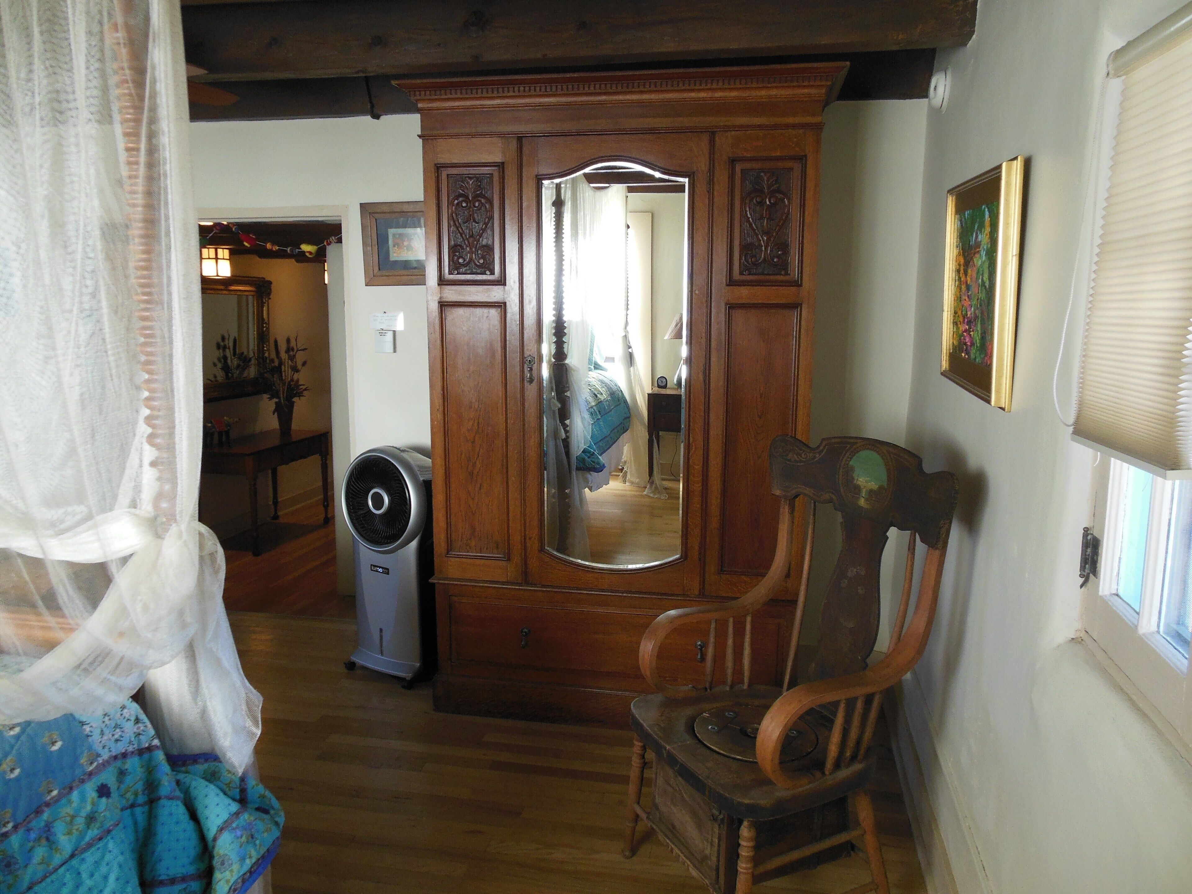 Una habitación con un armario de madera, un espejo, una silla y una cama con colcha azul.
