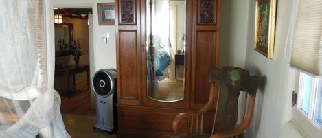 Una habitación con un armario de madera, un espejo, una silla y una cama con colcha azul.
