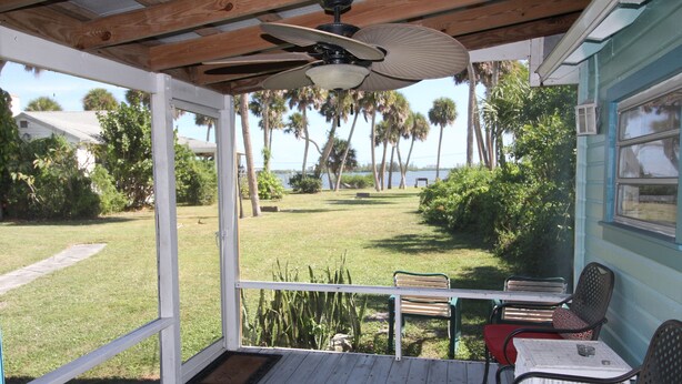 A covered porch with a ceiling fan, a table, and two chairs. - The Lodge, cozy one bedroom King Cottage on the Indian River Lagoon (Fort Pierce)