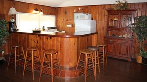 A kitchen with wooden paneling, a white refrigerator, a microwave, and bar stools. - The Lodge, cozy one bedroom King Cottage on the Indian River Lagoon (Fort Pierce)