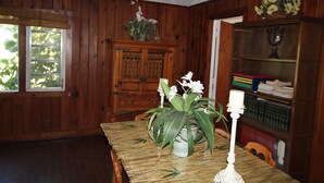 A wooden-paneled room with a dining table, a potted plant, a candelabra, and a bookshelf. - The Lodge, cozy one bedroom King Cottage on the Indian River Lagoon (Fort Pierce)