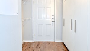 Un couloir avec une porte blanche, un plancher en bois et des armoires blanches dotées de poignées argentées.