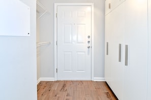 A hallway with a white door, wooden flooring, and white cabinets with silver handles.