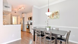 Une cuisine moderne dotée d’appareils électroménagers en acier inoxydable, un coin repas avec une table sombre et des chaises en métal, et un luminaire suspendu au-dessus de la table.