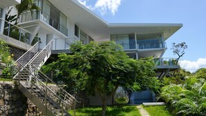 Ein modernes, mehrstöckiges Gebäude mit einer Treppe, die zu einem Balkon führt, umgeben von üppigem Grün und wolkenlosem, blauem Himmel.