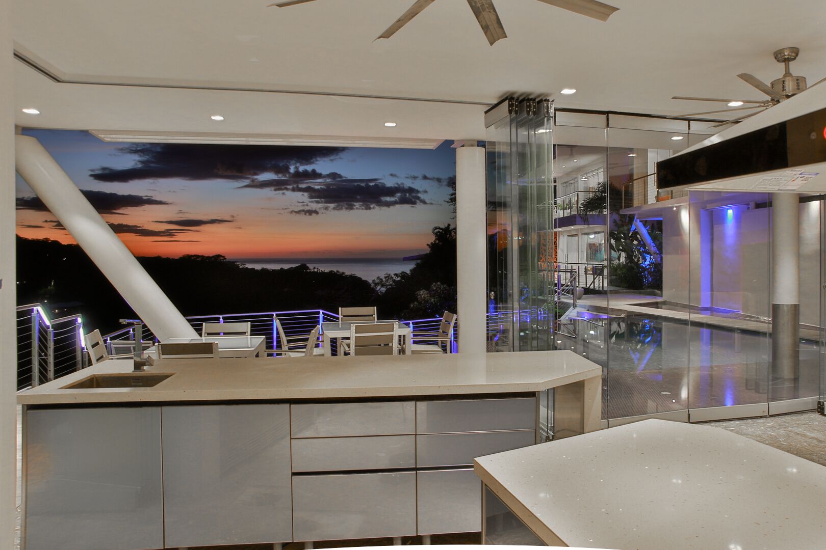 Un espace bar moderne agrémenté d’une fresque panoramique représentant un coucher de soleil, de rampes en verre et de mobilier contemporain.