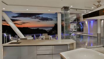 A modern bar area with a panoramic sunset mural, glass railings, and contemporary furniture.