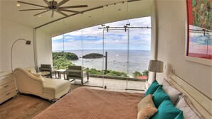 Ein Schlafzimmer mit einem großen Bett, einem Sessel, einem Schreibtisch und Meerblick.