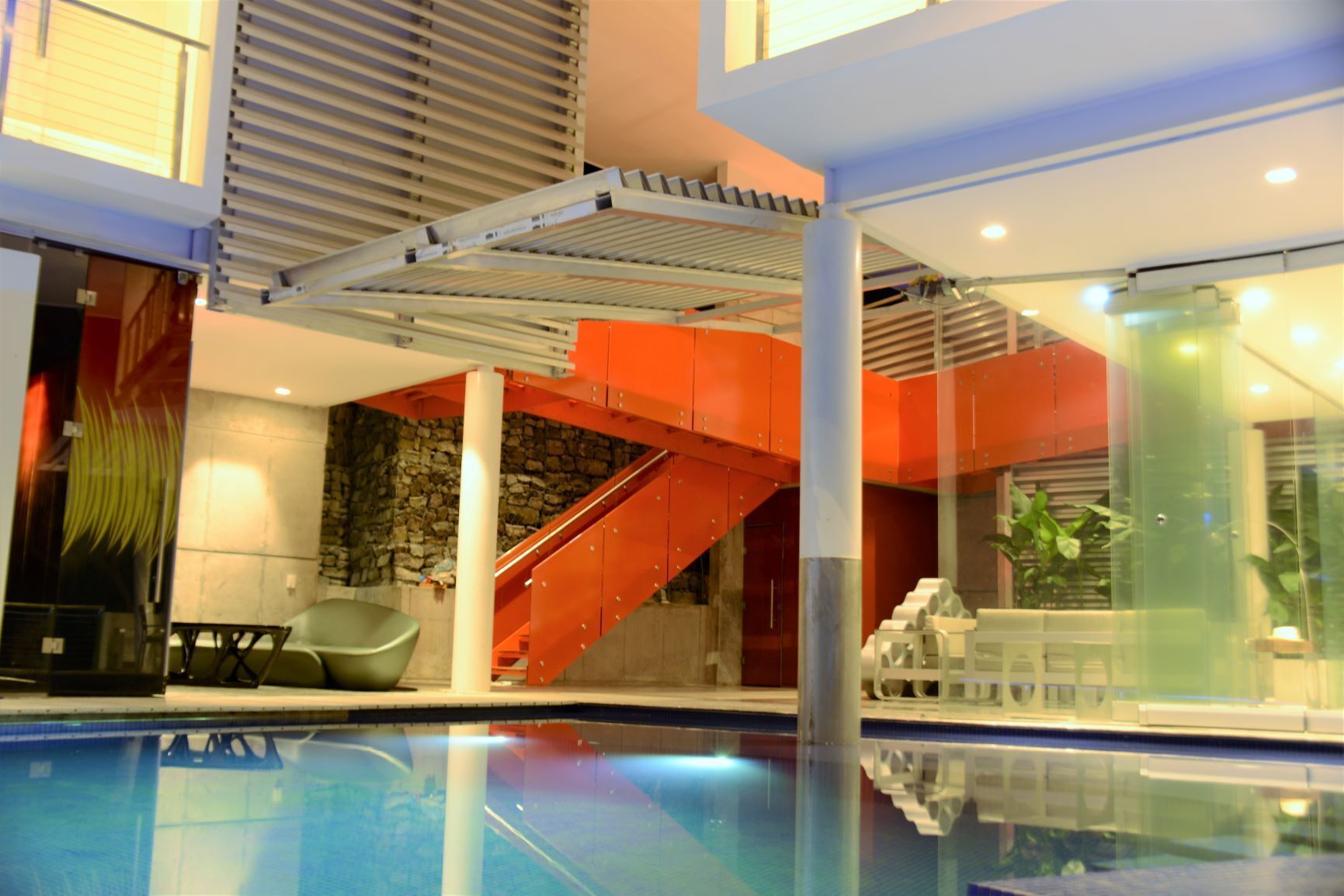 Una piscina interior amb una paret de vidre, una escala i una paret de pedra al fons.