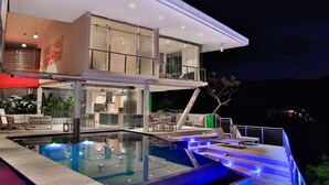 Ein modernes, zweistöckiges Haus mit einem verglasten Balkon, einem Schwimmbad und Sitzgelegenheiten im Freien.