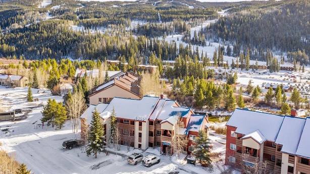 A lodge with multiple buildings, a parking area, and a snowy forested backdrop.