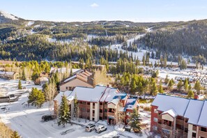 Et lodge med flere bygninger, en parkeringsplads og en skovklædt baggrund dækket af sne.