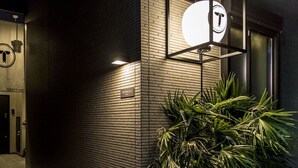 A building facade with a brick wall, a sign reading "TATERU Inn," and a large illuminated sign with a logo. - Trip Pod Chiyo A (Fukuoka)