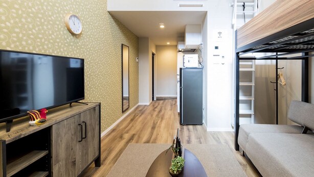 A modern living room with a flat-screen TV, a sofa, a wooden cabinet, and a small plant. - Trip Pod Chiyo A (Fukuoka)