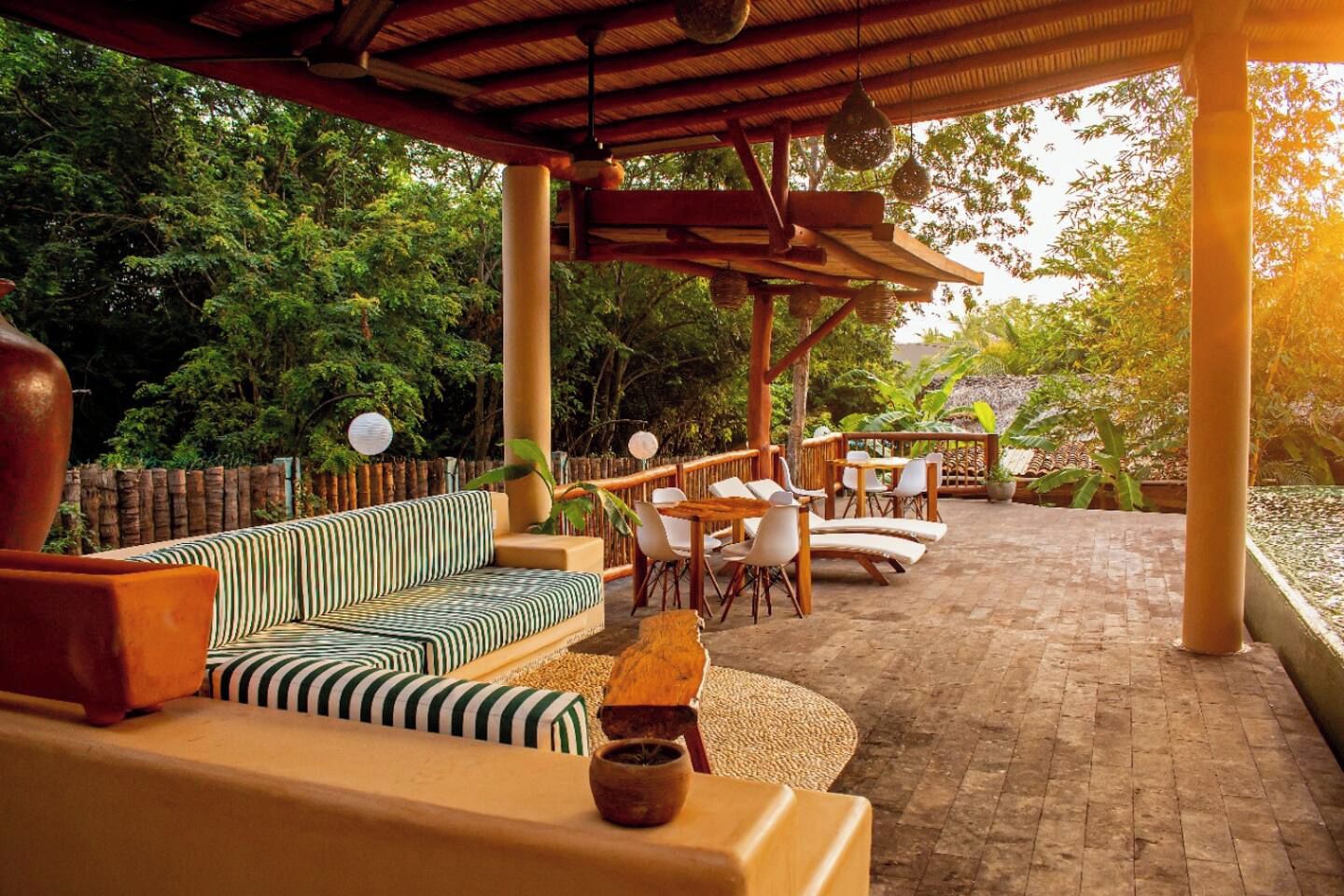 An outdoor patio with a wooden pergola, striped sofa, and white chairs.