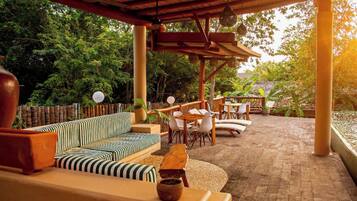 An outdoor patio with a wooden pergola, striped sofa, and white chairs.