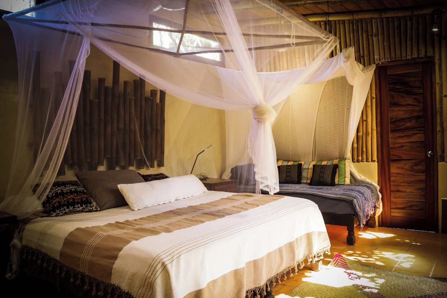 A room with a bed under a canopy, a bedside table, and a door with a wooden panel.