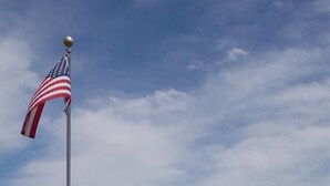 Een woonwijk met twee tweelaagse huizen, een vlaggenmast met de Amerikaanse vlag, een bord met daarop 'zwemmen verboden' en een wateroppervlak dat de gebouwen weerspiegelt.