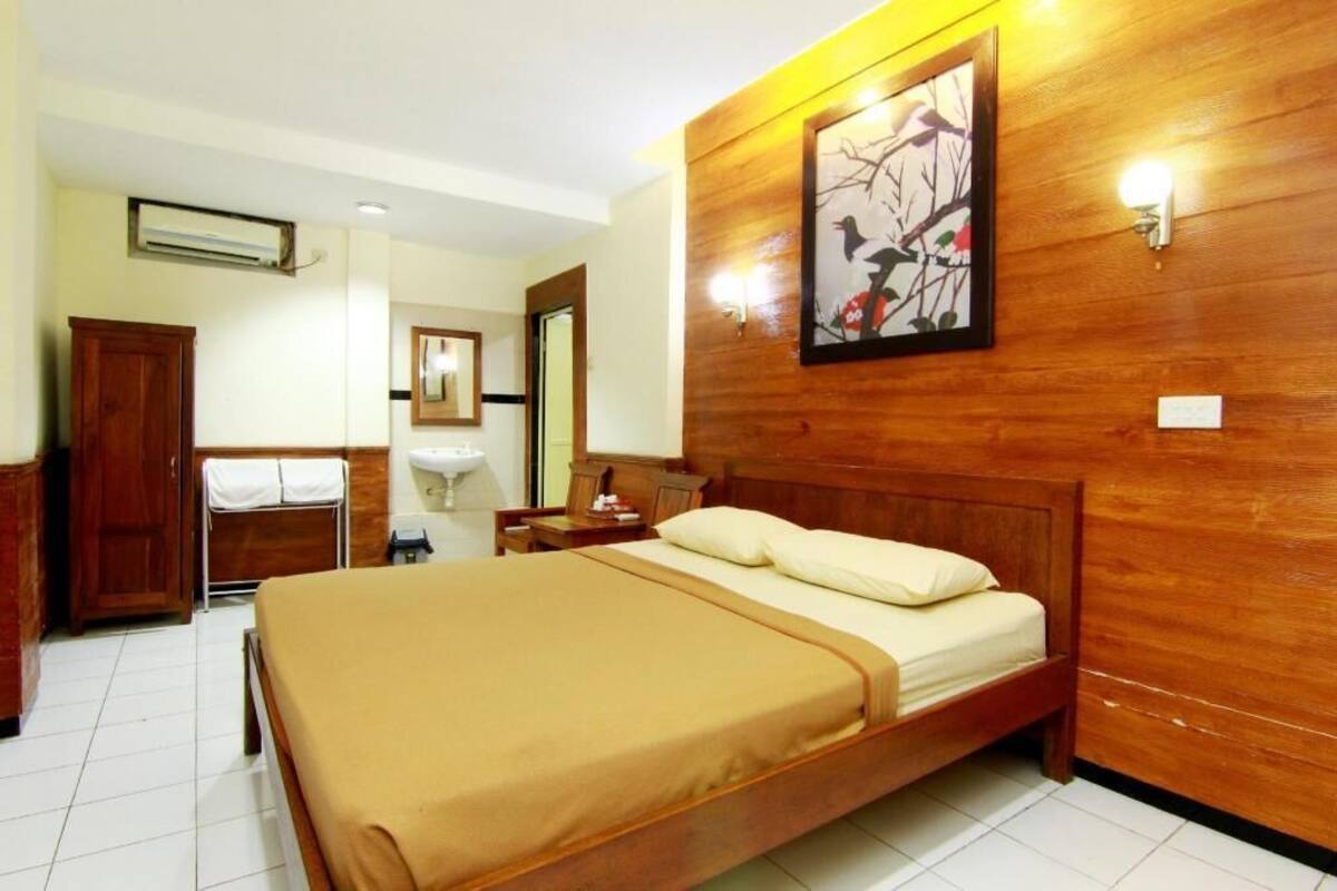 Habitación de hotel con cama de madera, mesita de noche, espejo, armario y aire acondicionado instalado en la pared.