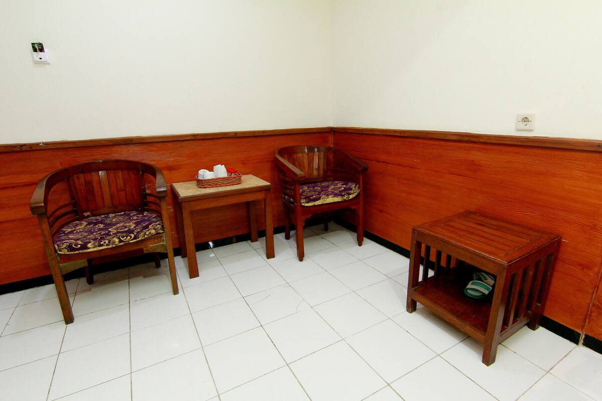 Habitación de esquina con dos sillas de madera, una mesita pequeña y una mesita auxiliar de madera.