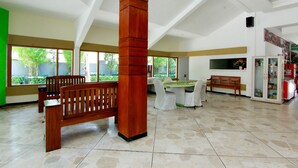 A spacious room with a high ceiling, a wooden bench, a dining table with chairs, and a refrigerator. - The Soemarsono Hotel (Depok)