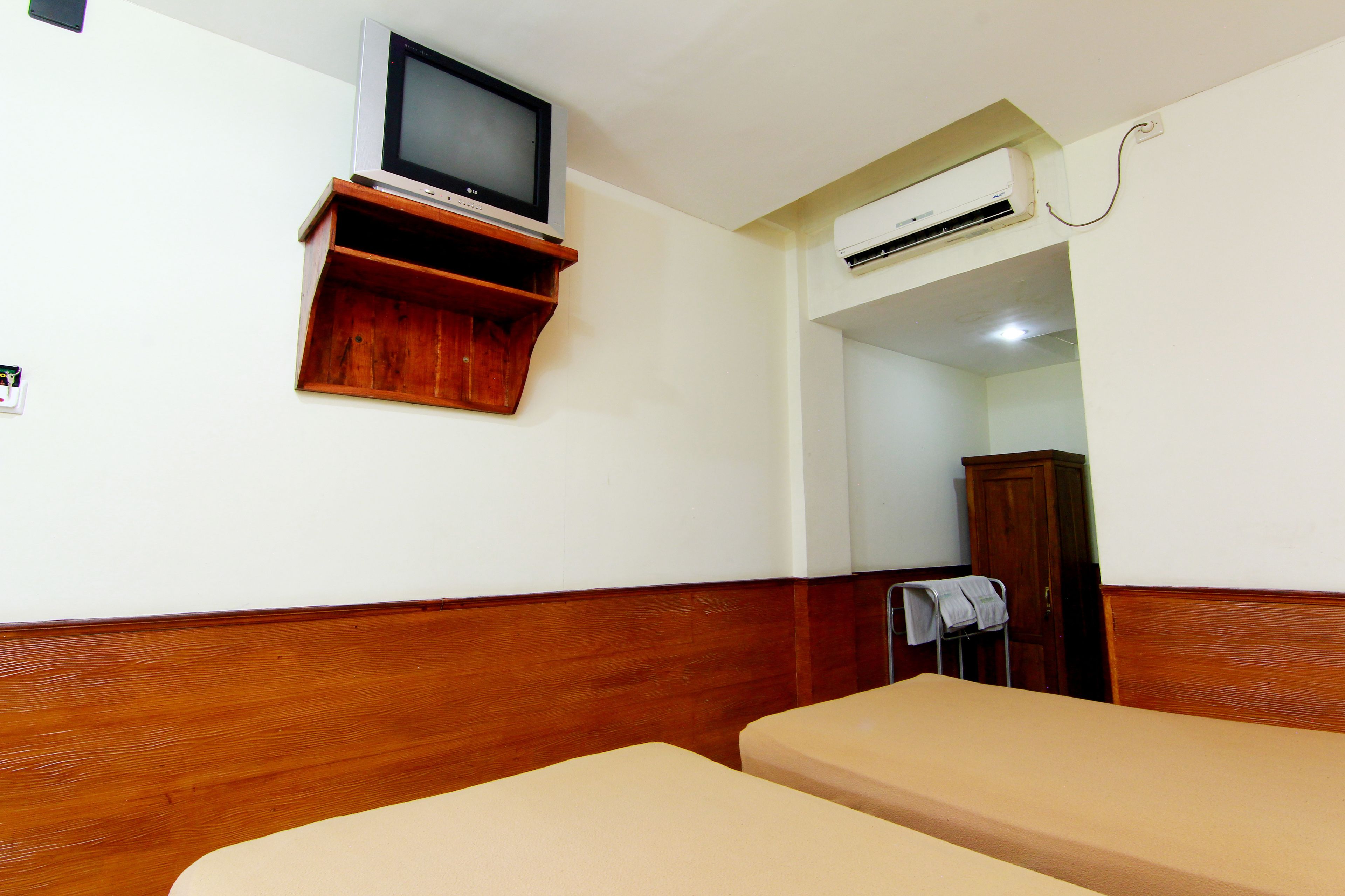 Habitación de hotel con dos camas individuales, cabecera de madera, un televisor sobre una estantería de madera y un equipo de aire acondicionado.