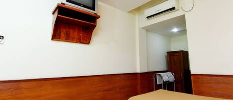Habitación de hotel con dos camas individuales, cabecera de madera, un televisor sobre una estantería de madera y un equipo de aire acondicionado.