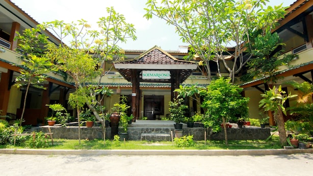 A traditional building with a covered entrance, potted plants, and a stone wall. - The Soemarsono Hotel (Depok)