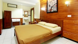 A hotel room with a large bed, wooden walls, a wooden wardrobe, a bedside table, a nightstand, a mirror, and a wall-mounted light fixture. - The Soemarsono Hotel (Depok)