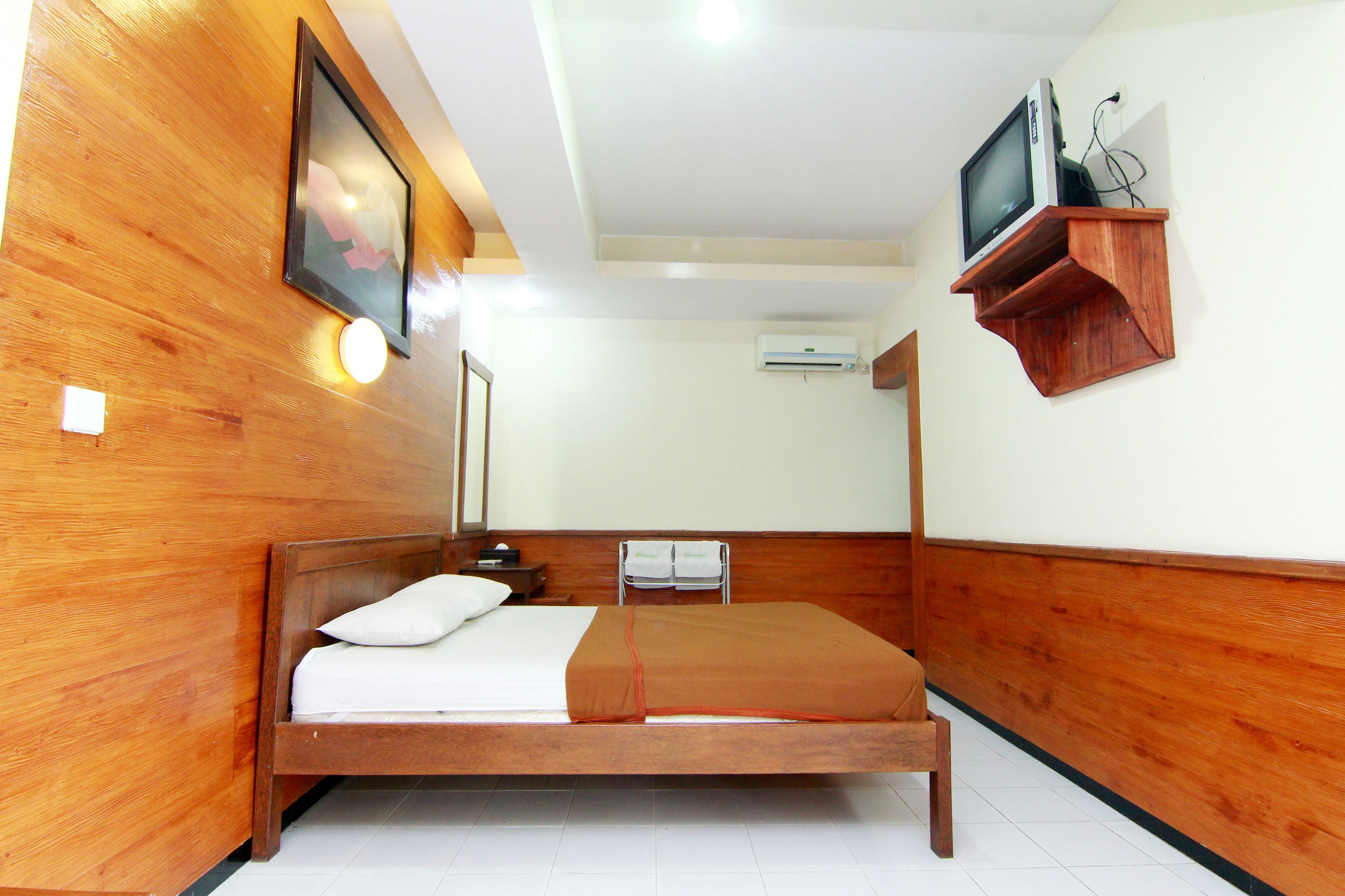 A wooden-paneled room with a bed, a television on a shelf, and a wall-mounted air conditioner.