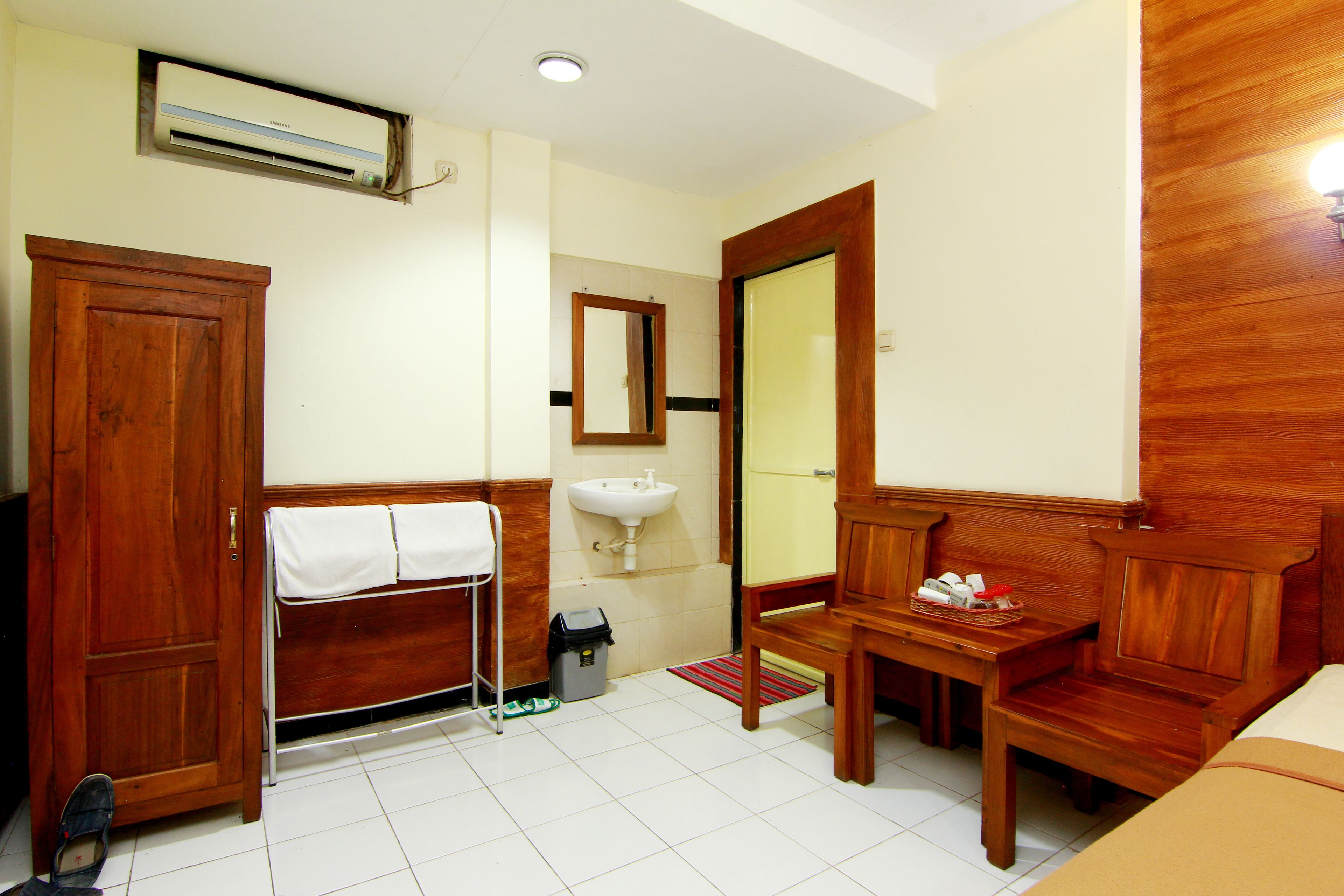 Habitación de hotel con armario de madera, lavabo, espejo, mesita con artículos de aseo y cama.