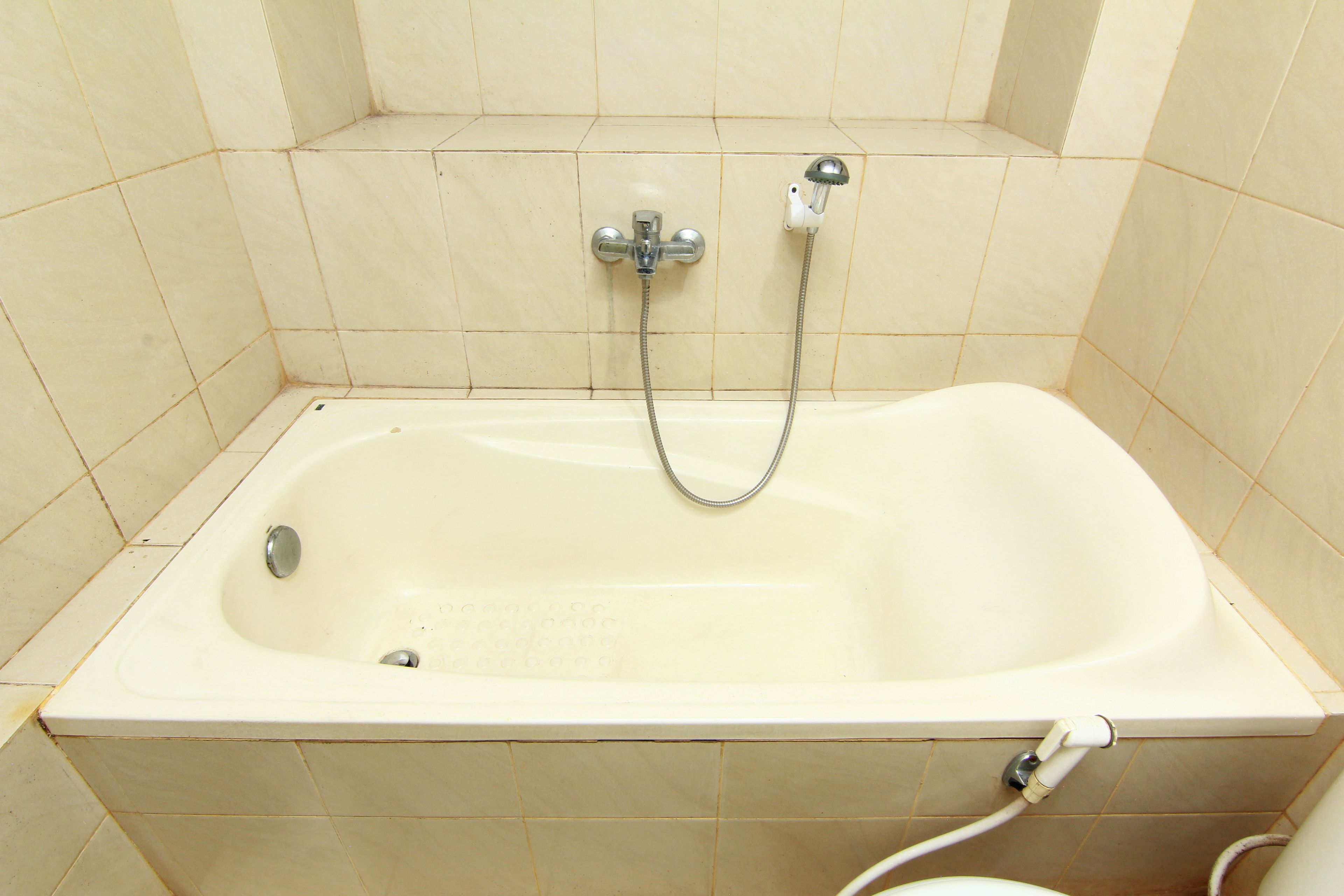 A standard bathtub with a showerhead and hose, set in a tiled bathroom.