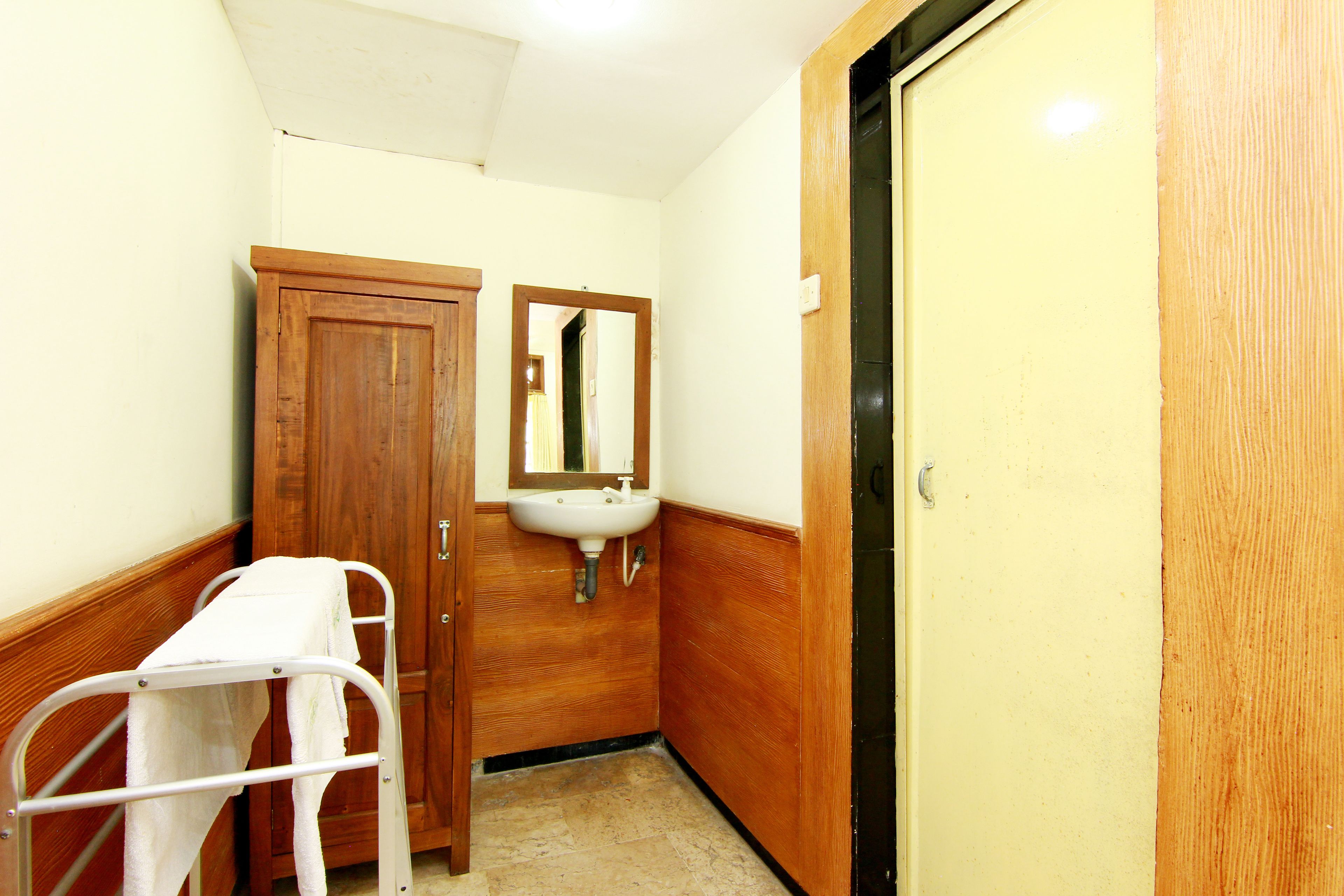 A narrow bathroom with a wooden door, a white sink, and a mirror.
