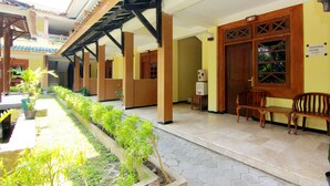 A covered outdoor area with wooden benches and a planter with green plants. - The Soemarsono Hotel (Depok)