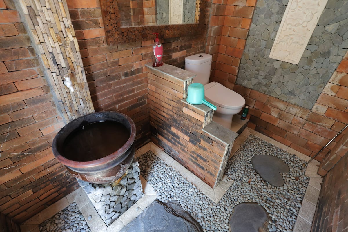 A bathroom with a brick wall, a toilet, a large basin, and a stone floor.