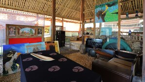 Un interior con techo de bambú, una mesa con mantel negro y obras de arte en las paredes.