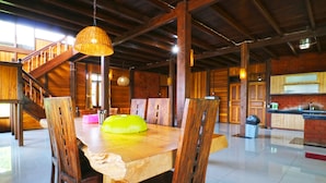 A spacious dining area with a wooden table and chairs, a staircase, and a kitchen in the background.