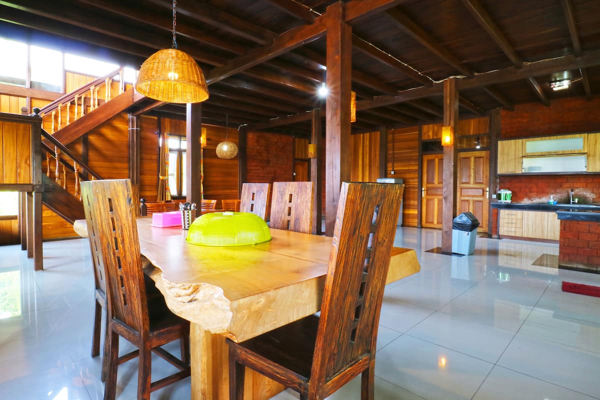 Un vaste espace dédié à la salle à manger, avec une table et des chaises en bois, un escalier et une cuisine en arrière-plan.