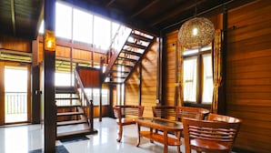 A wooden interior with a staircase, a dining area with chairs and a table, and a hanging light fixture.