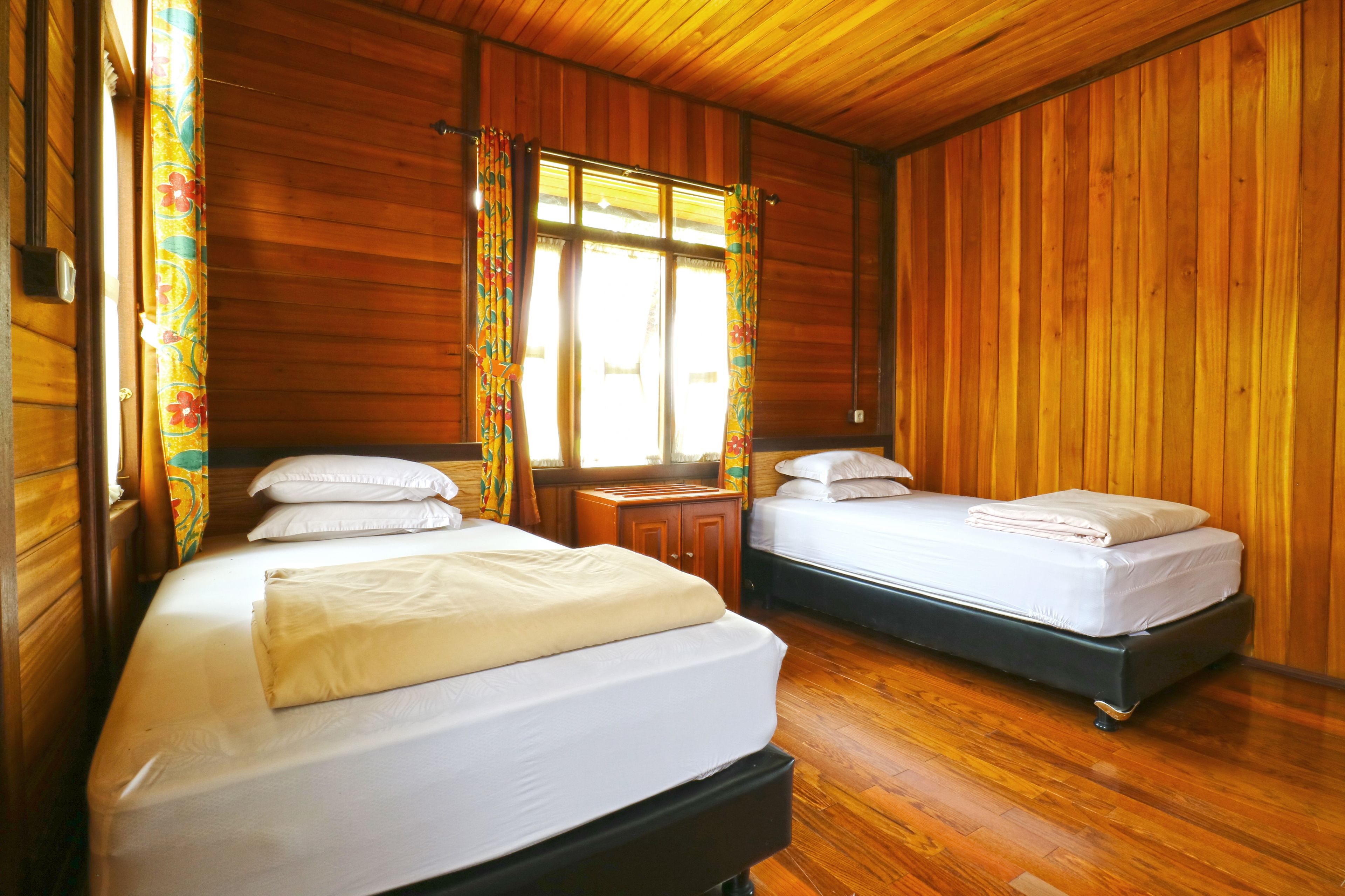 Une chambre de chalet en bois avec deux lits, un plafond en bois et une fenêtre avec des rideaux.