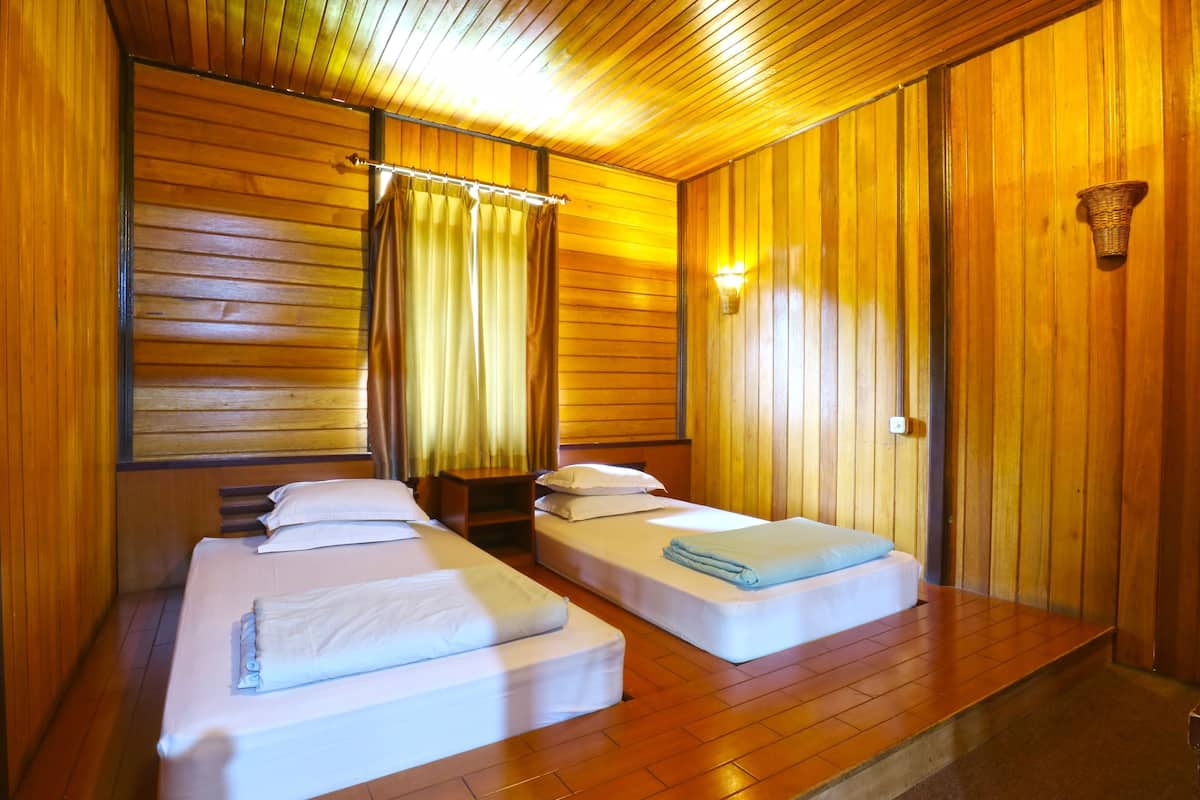 Une chambre avec deux lits, des murs en bois, une fenêtre avec des rideaux, une table de chevet et un luminaire fixé au mur.