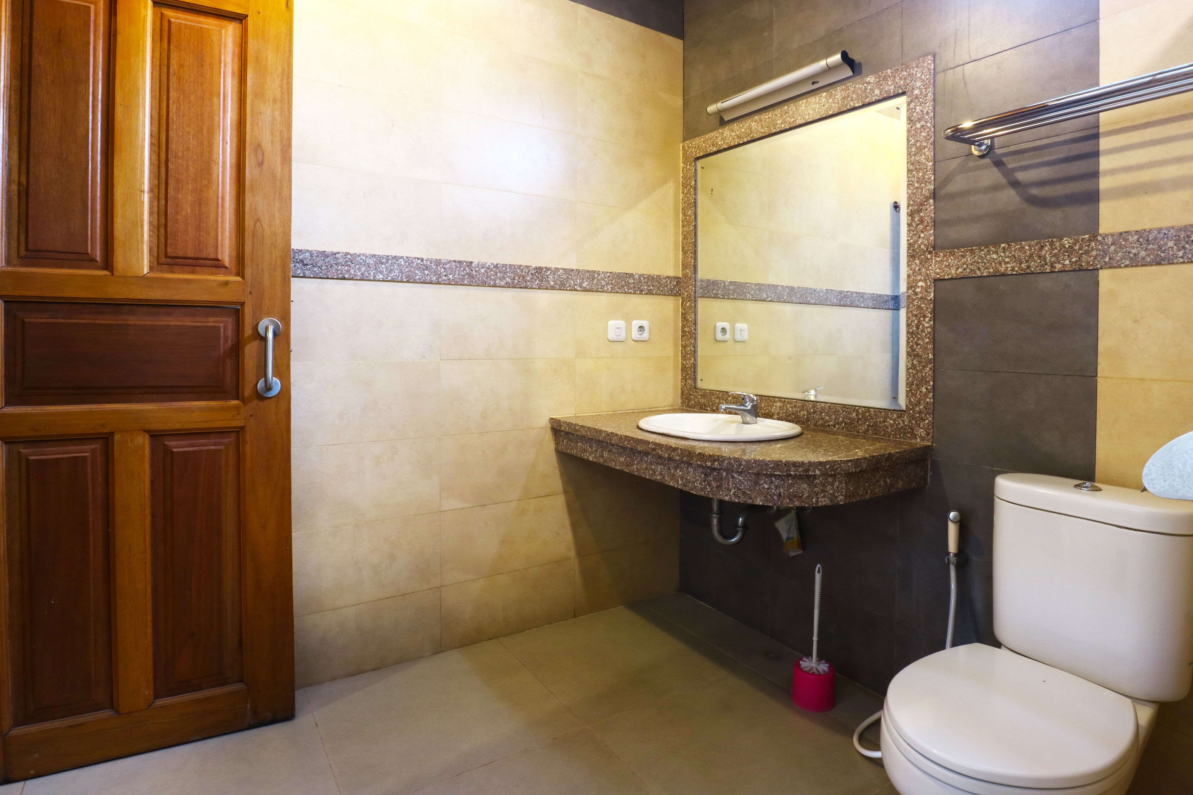 A bathroom with a wooden door, a sink with a mirror, a toilet, and a hand dryer.