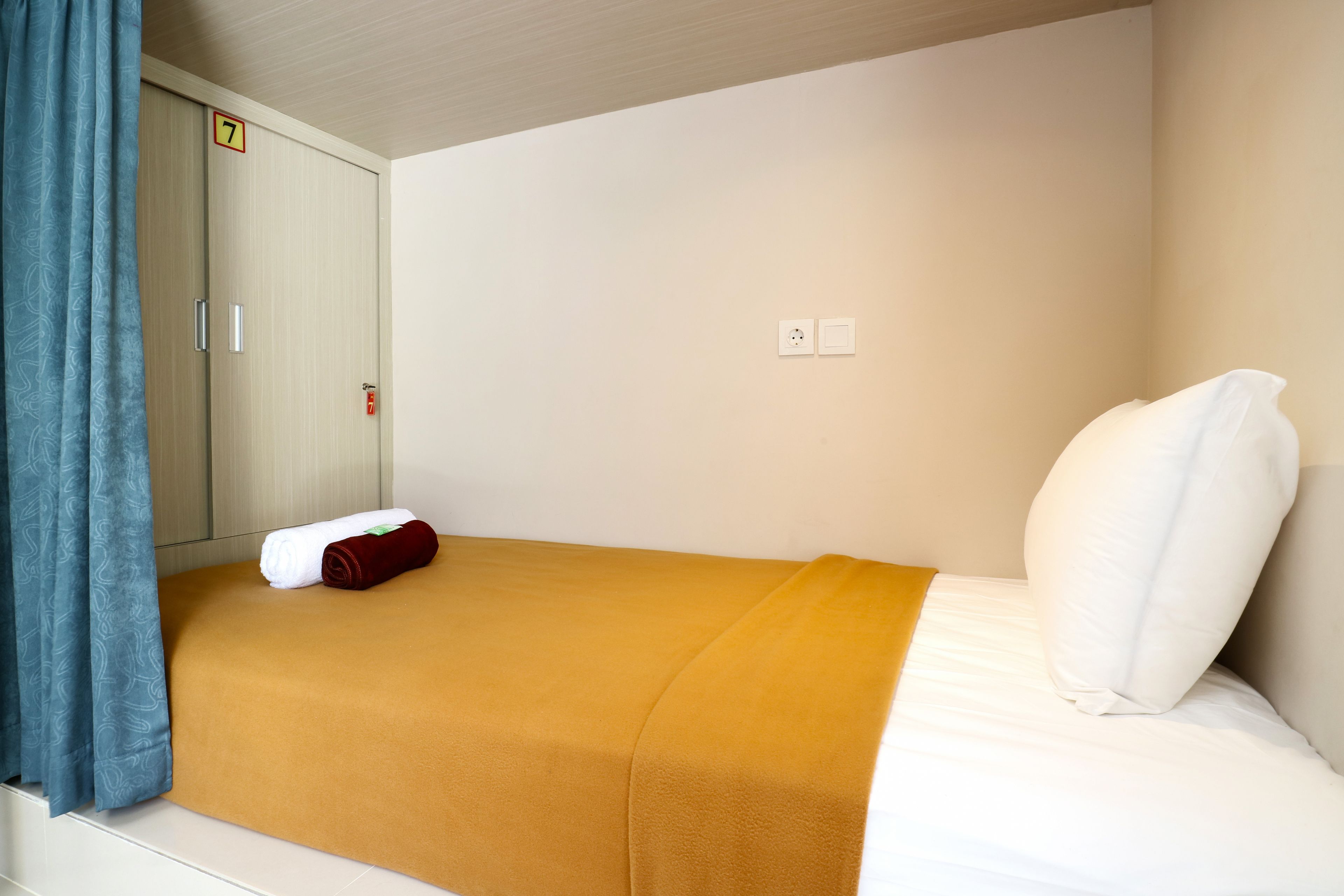 Una cama individual con una colcha marrón, almohadas blancas y una cortina azul.