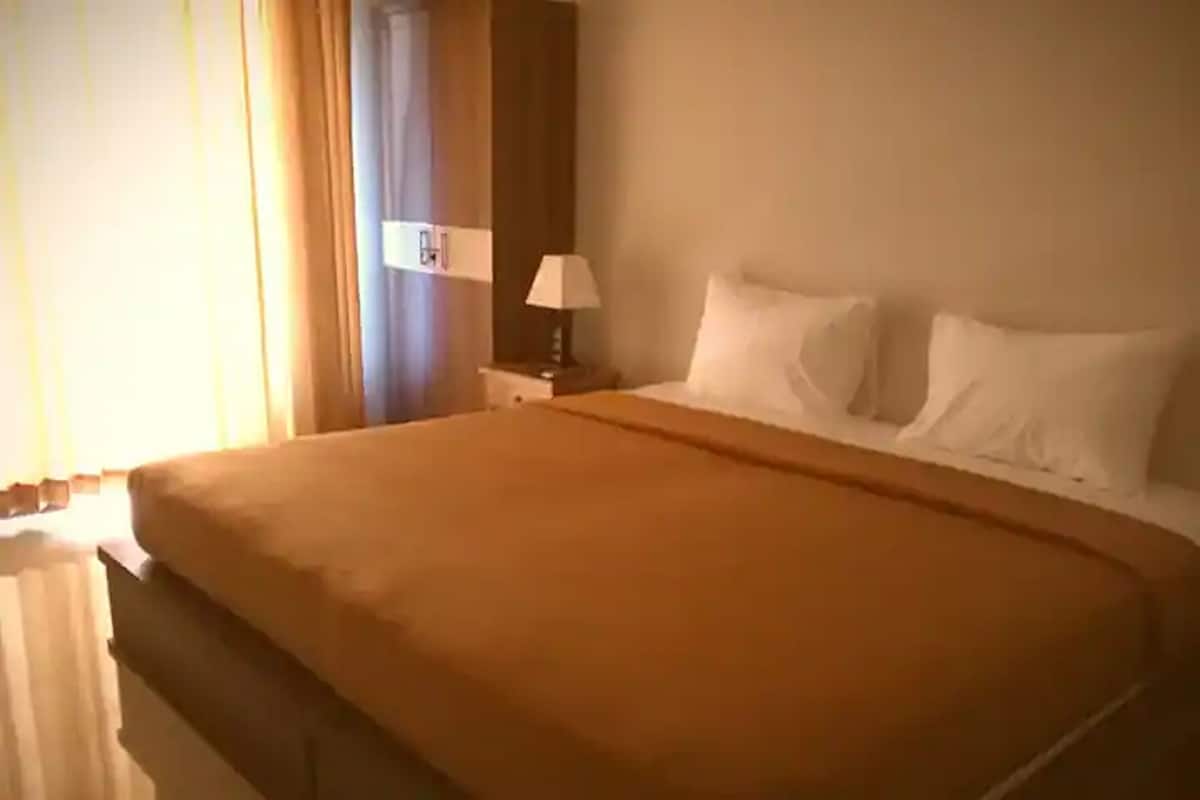 A hotel room with a large bed, a nightstand with a lamp, and a window with curtains.
