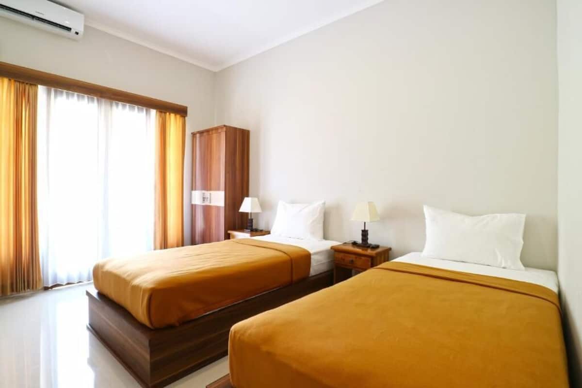 A hotel room with two beds, a wooden wardrobe, and a window with curtains.