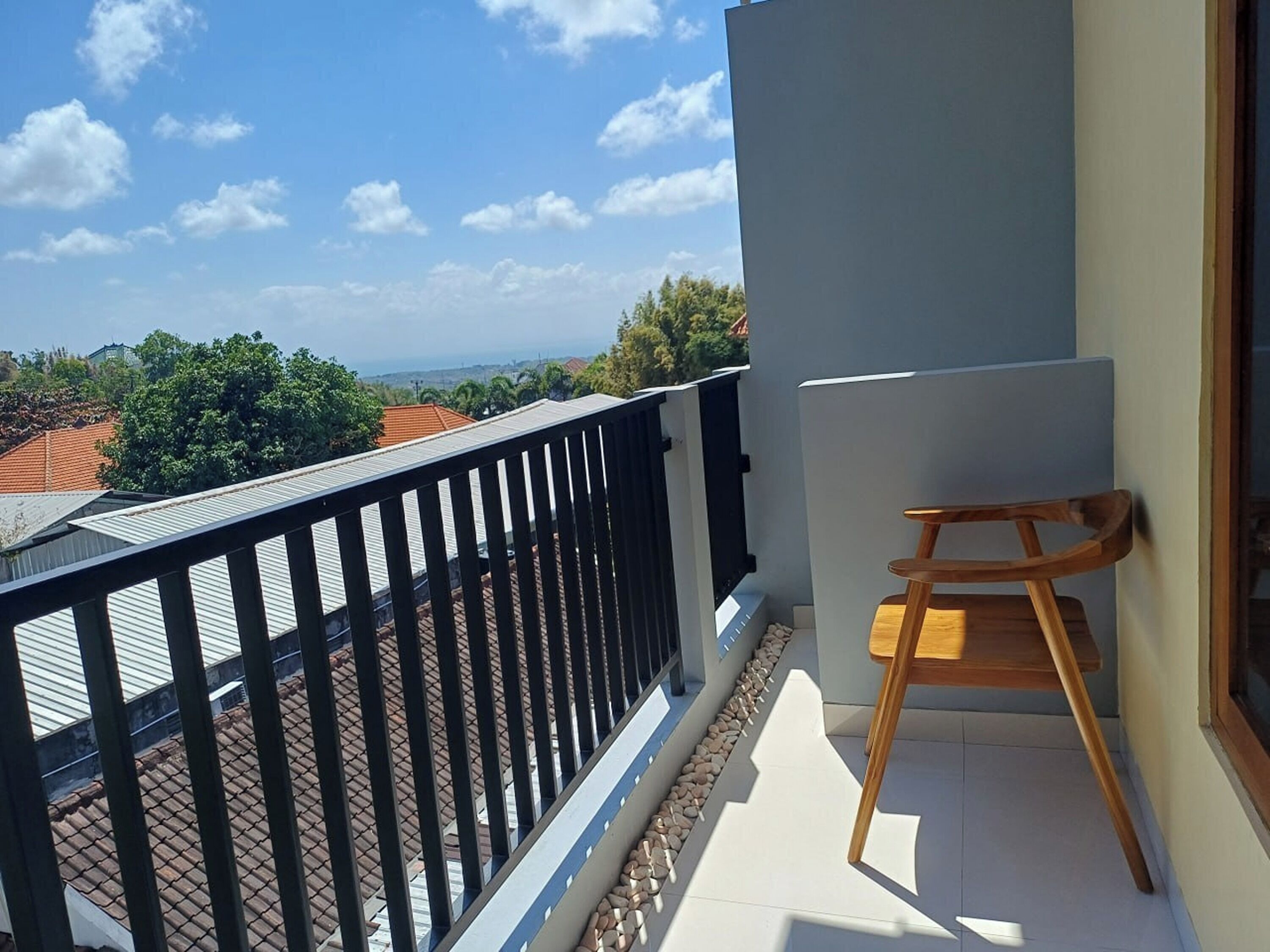 Un balcón con vista al mar y edificios, una silla de madera y piso de baldosas.